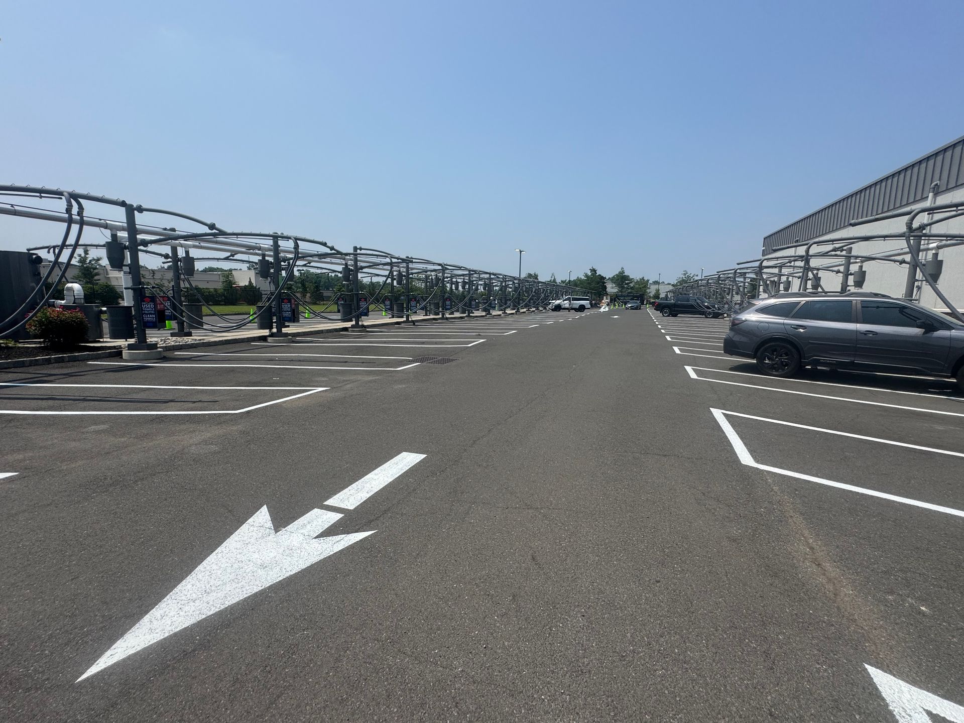 Asphalt car wash lot with directional arrow, car wash stations, and vehicles on a sunny day.