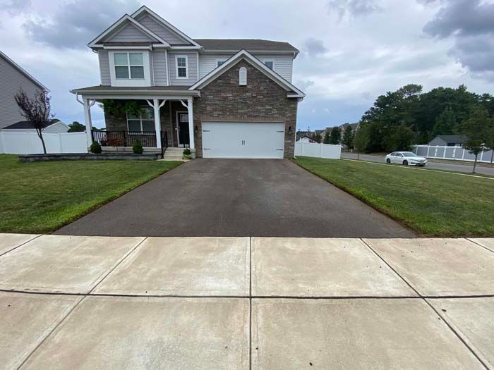 Two-story gray house with driveway, grass, and sidewalk. White garage door. Overcast sky.