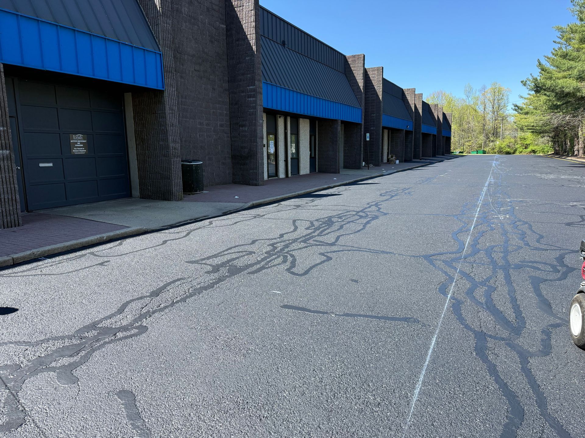 Empty parking lot beside a row of dark industrial buildings under a blue sky.