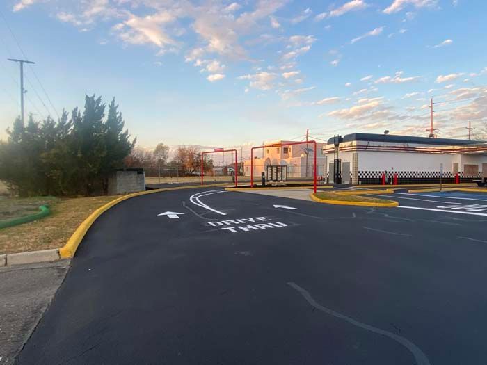 Drive-thru lane at a fast-food restaurant. Black asphalt with white arrows and text against a blue sky.