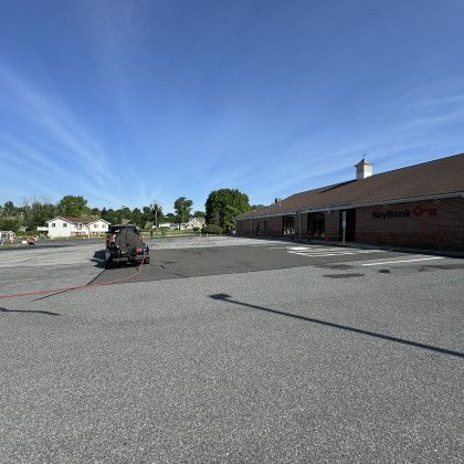 Empty parking lot in front of a brick building under a blue sky. A vehicle is in the lot.
