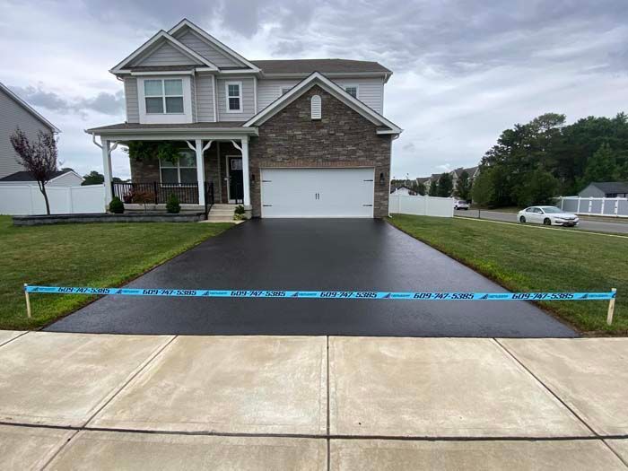 Newly paved driveway in front of a two-story gray house, blocked off with blue tape.