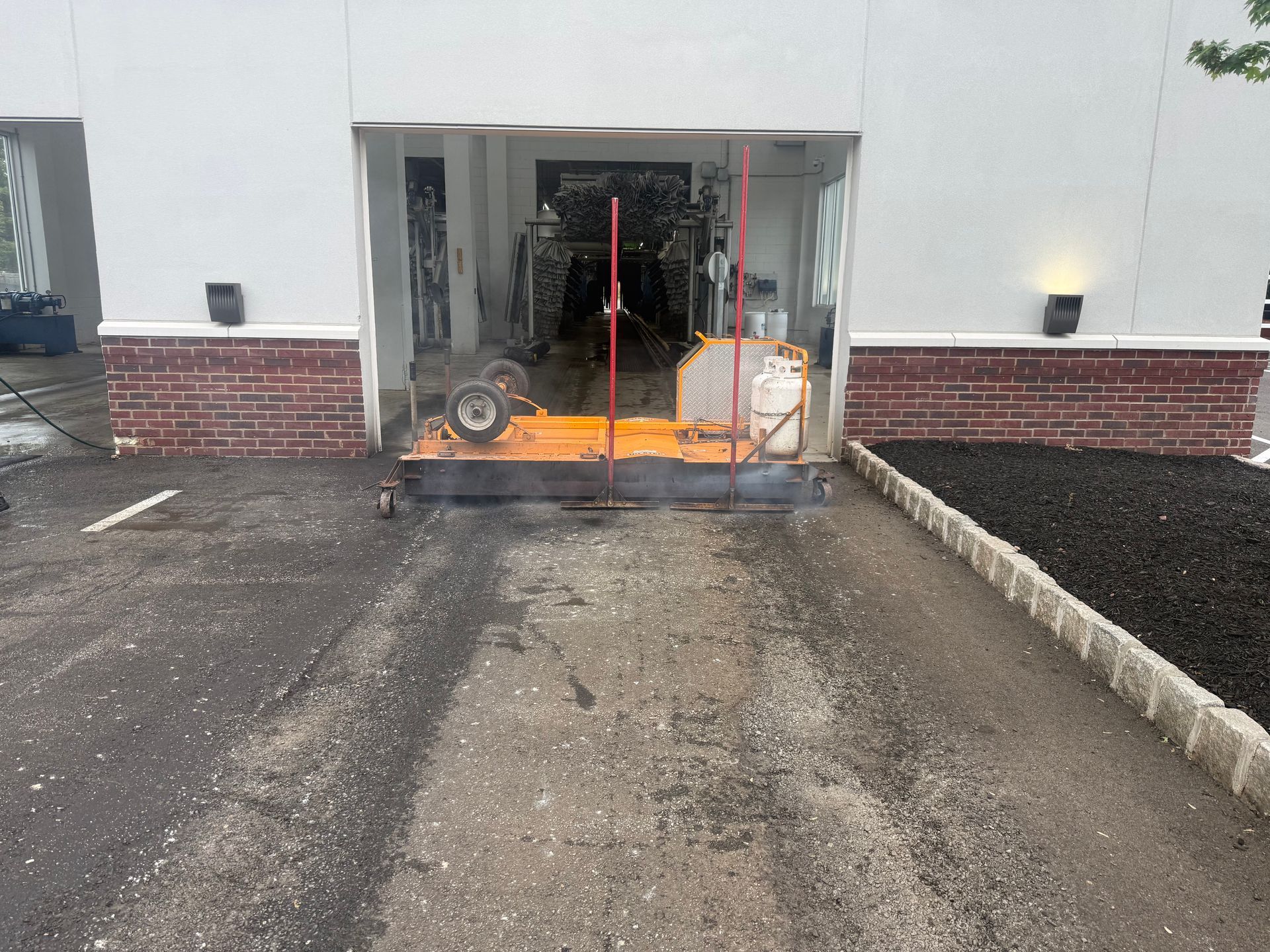 Damaged storefront entrance with fire inside, orange flames and smoke behind a metal barrier, parking lot in front