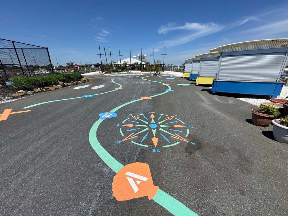A paved outdoor path with colorful markings, including a compass rose, leading toward buildings under a bright blue sky.