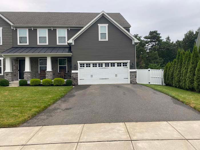 Gray house with white garage door, asphalt driveway, and green lawn.