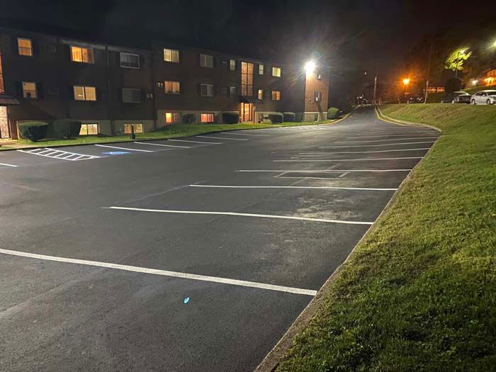 Nighttime view of an empty parking lot in front of a multi-story building. Illuminated by streetlights.
