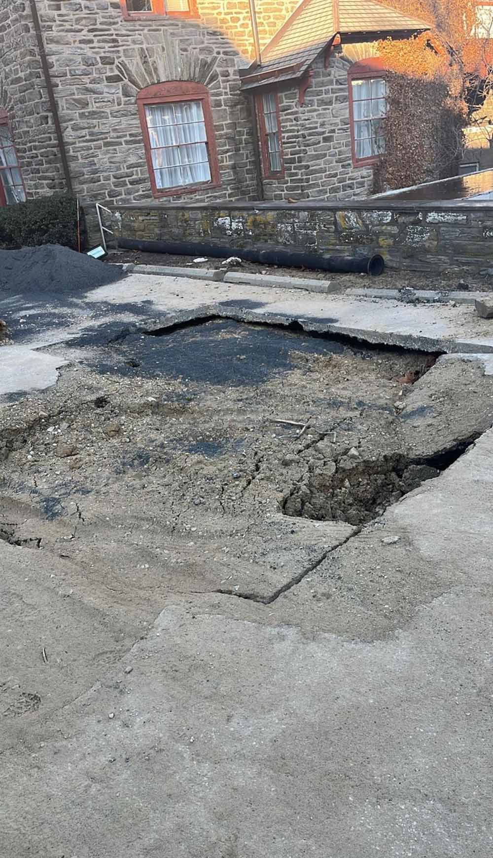 A large hole in a paved surface, in front of a brick building.