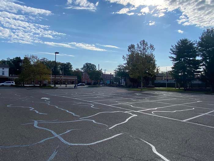 Cracked asphalt parking lot under a blue sky, trees in the distance, a few vehicles parked.