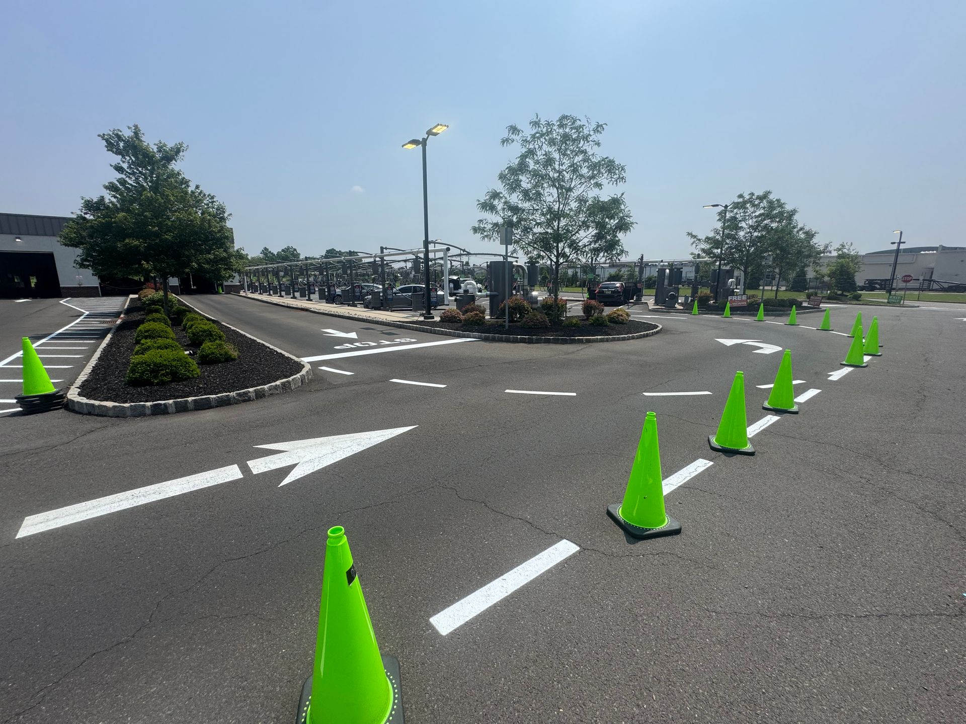 Bright green traffic cones line an asphalt road with white directional arrows, sunny day.