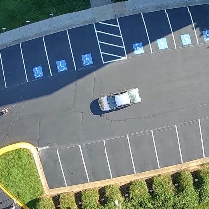 Aerial view of a parking lot with blue handicap parking spaces. A silver car is parked in a space.