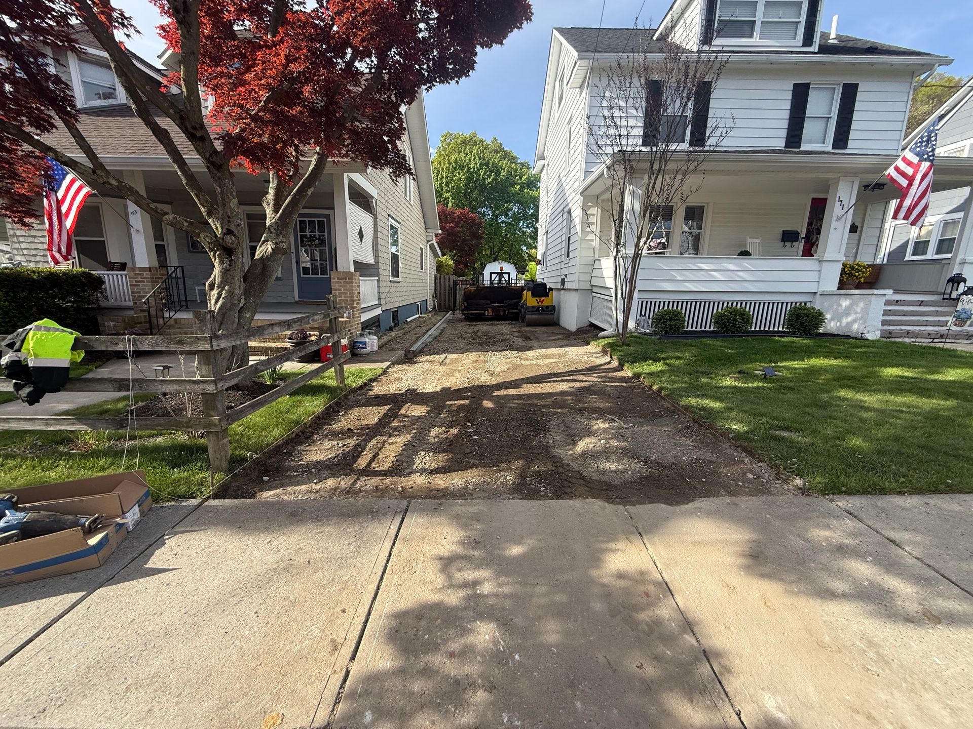 Two white houses with American flags and a dirt path between them, viewed from a sidewalk