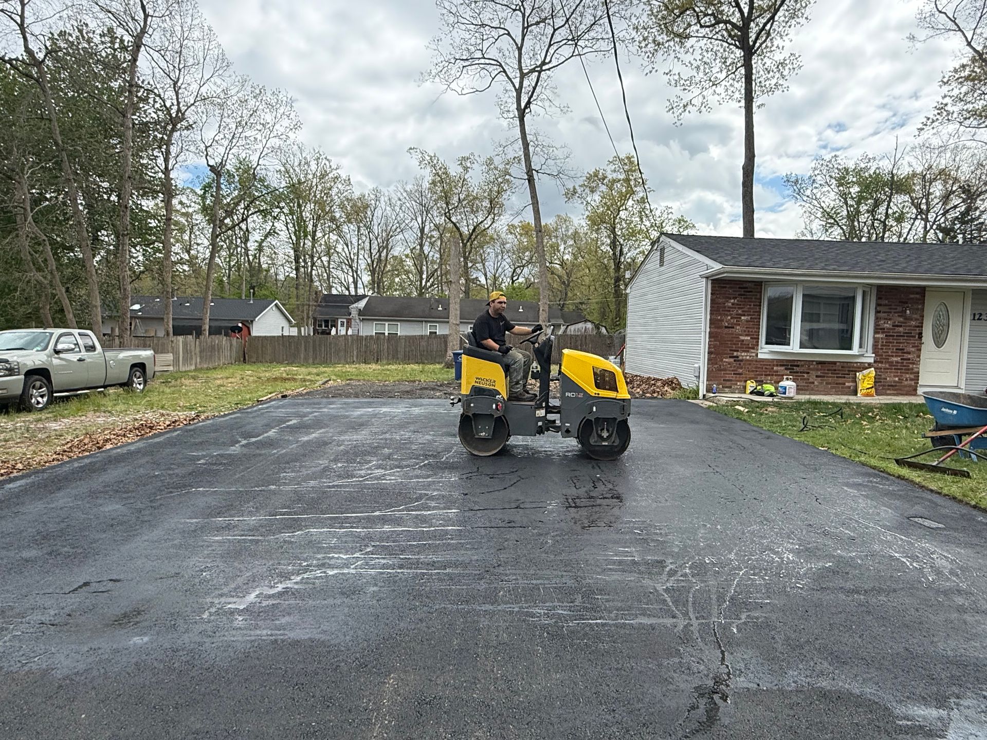 Person mowing a wet driveway with a yellow riding mower beside a brick house