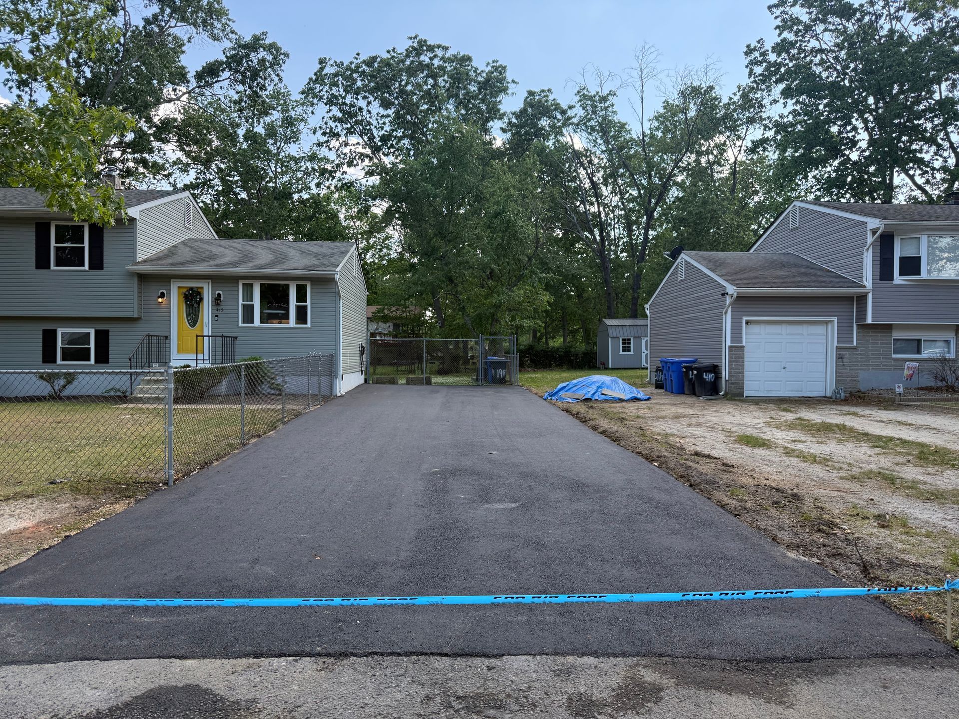 Gravel driveway between two houses, with a blue tape line across the front edge.