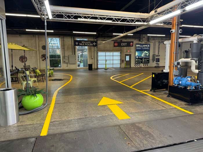 Entrance of a car wash with yellow lines and arrow, seating area, and exit signs.