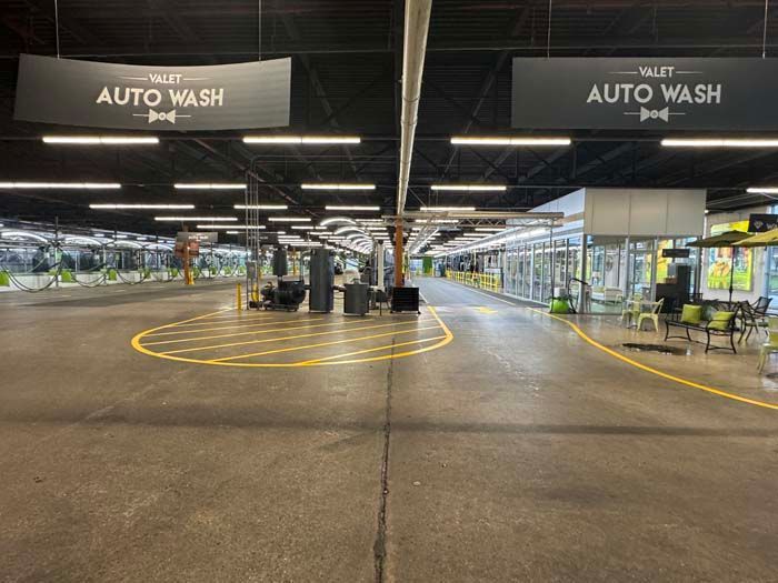 Large indoor auto wash facility with yellow markings, signage, and equipment.