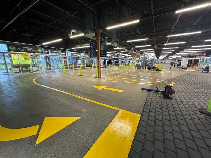 Yellow arrows mark a path toward security at an airport with a dark ceiling and glass entrances.