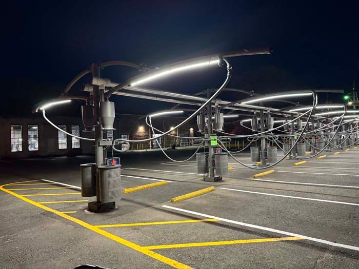 Parking lot with multiple self-service car wash bays illuminated by overhead LED lights at night.
