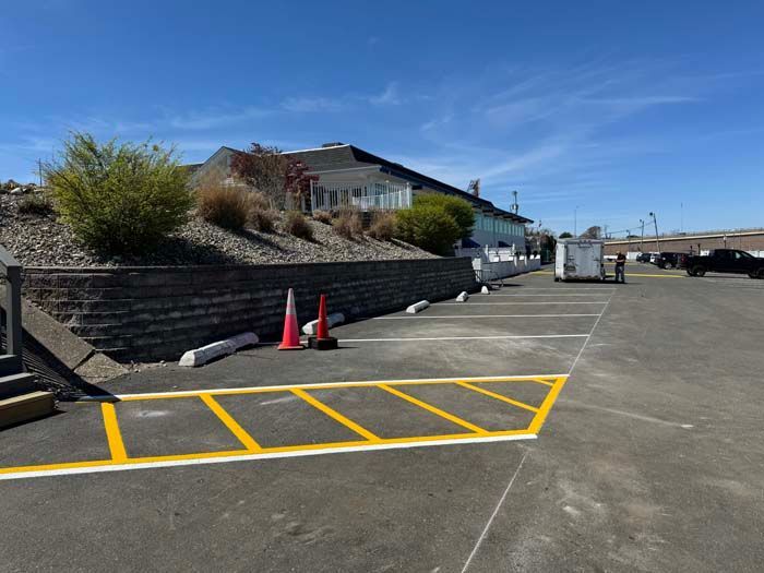 Parking lot with painted yellow lines, building on a hill, blue sky.