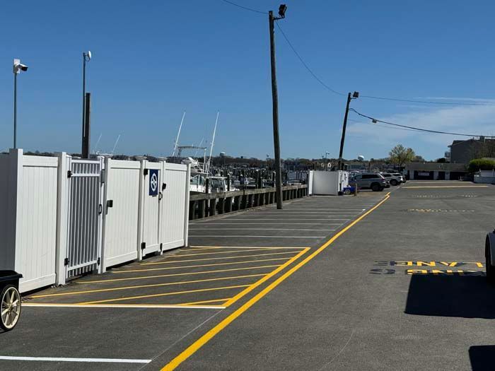 Parking lot with white fences, boats at a dock, and a clear blue sky.