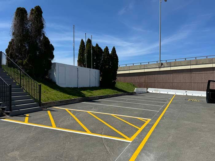 Empty parking lot with yellow lines, stairs, and a wall under a blue sky.