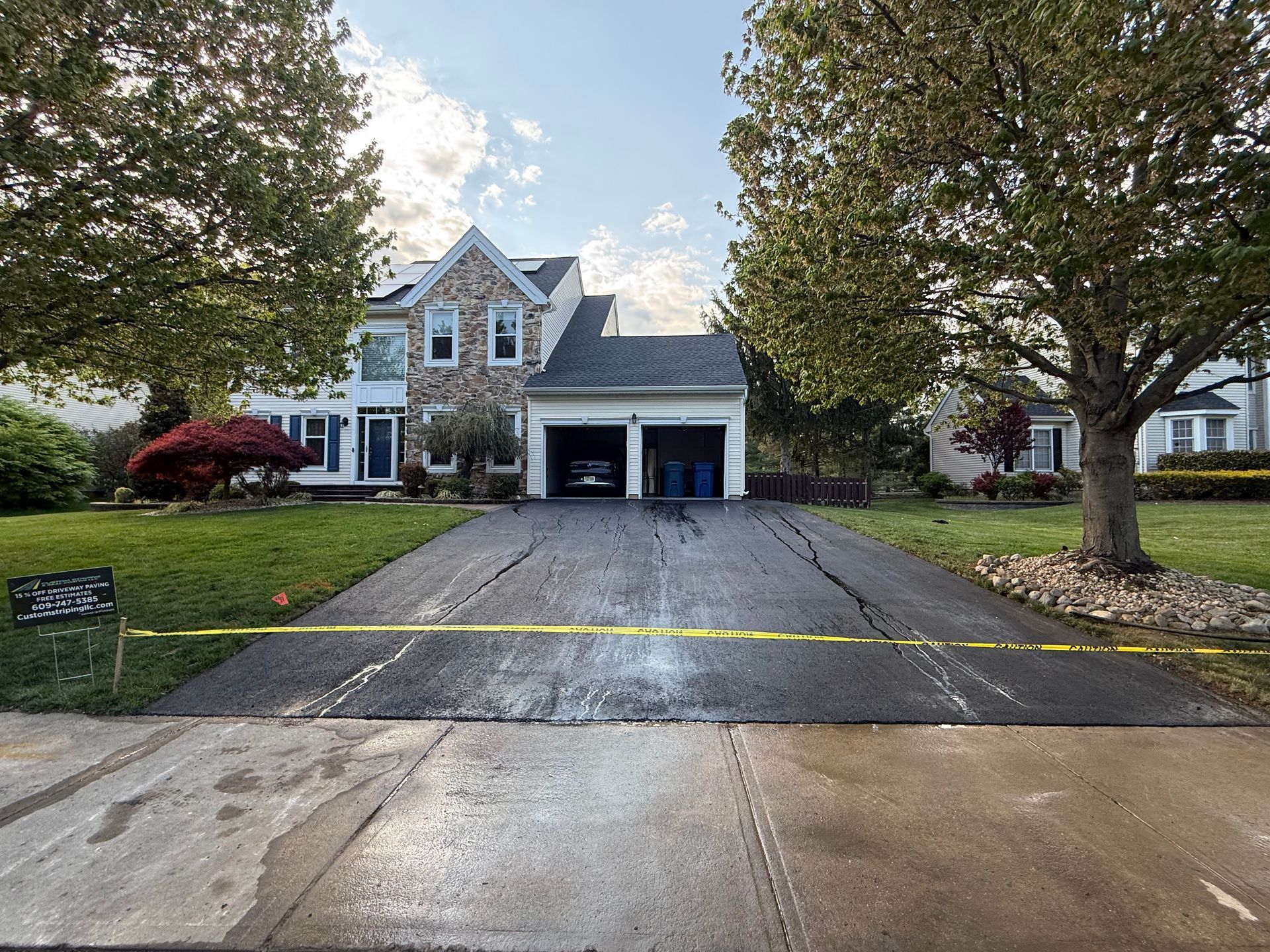 Suburban two-story house with a wet driveway, front lawn, and trees lining the street