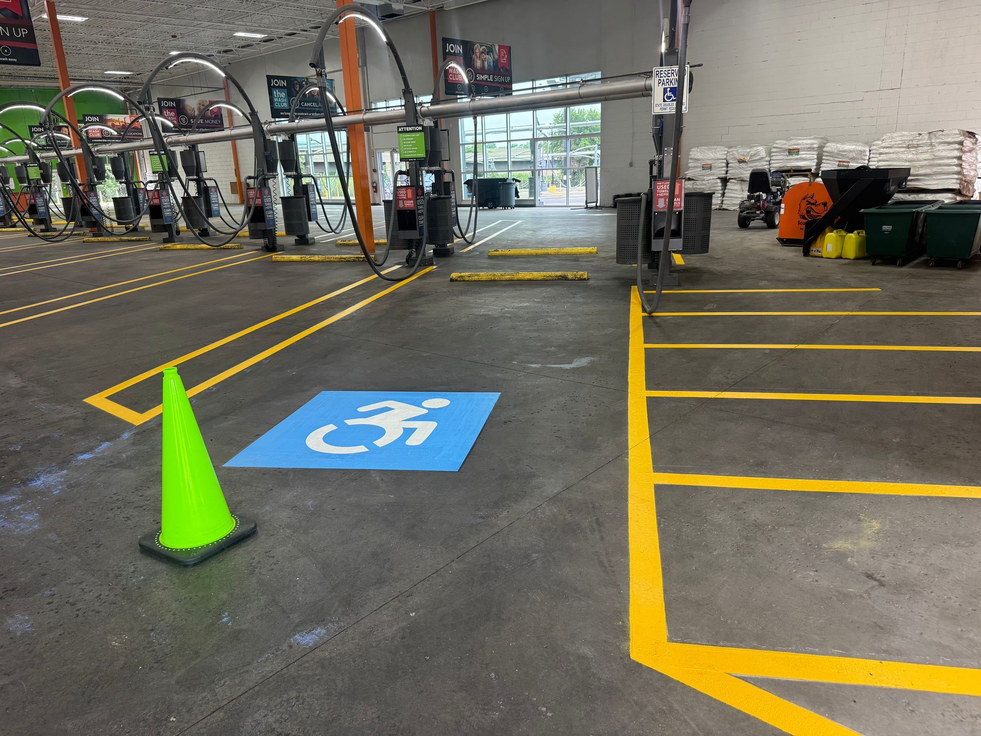 Indoor parking area with accessible parking spot, marked with blue wheelchair symbol and yellow lines. Cone present.