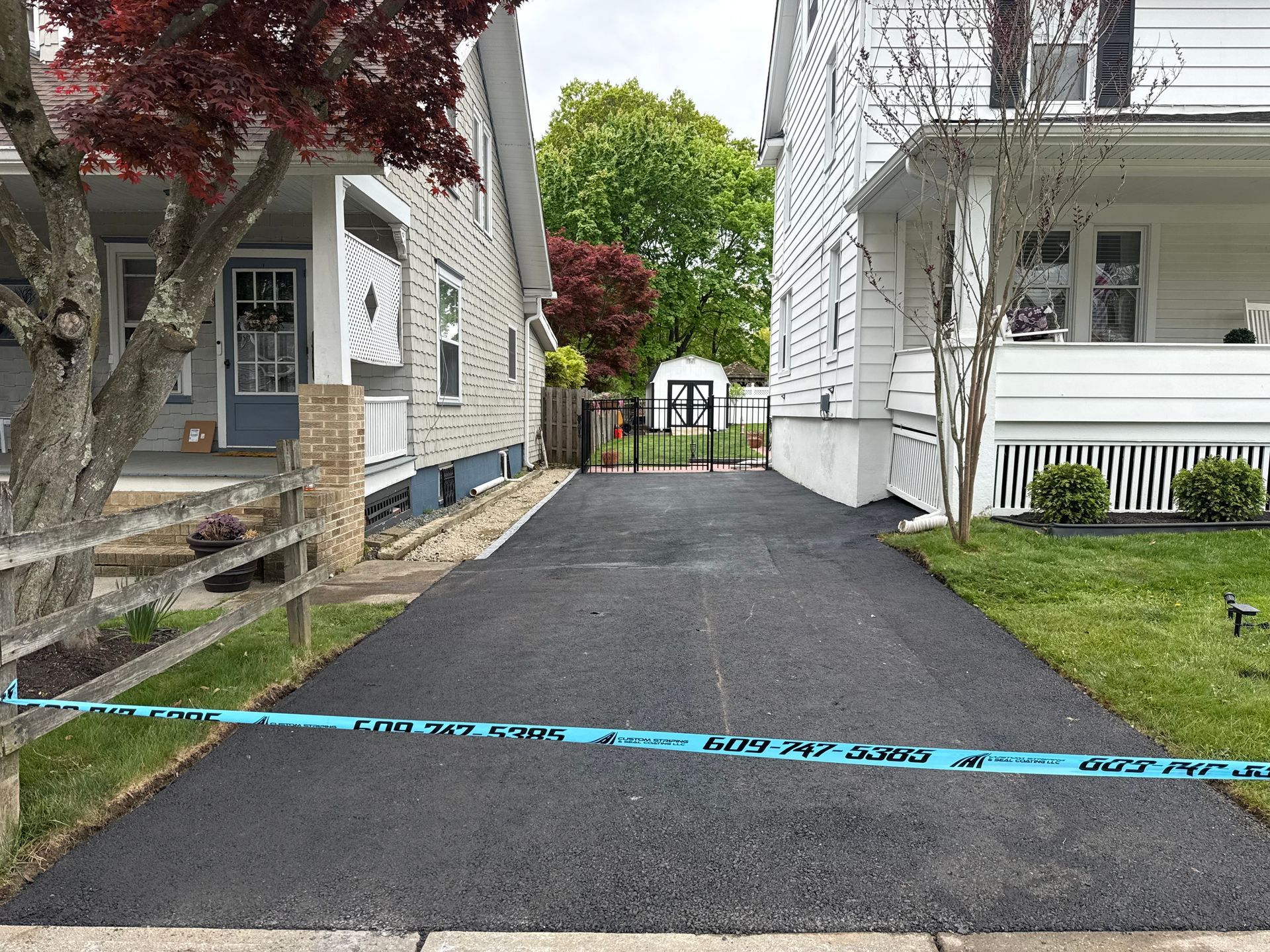 Narrow paved driveway between two houses, blocked by blue police tape at the entrance.