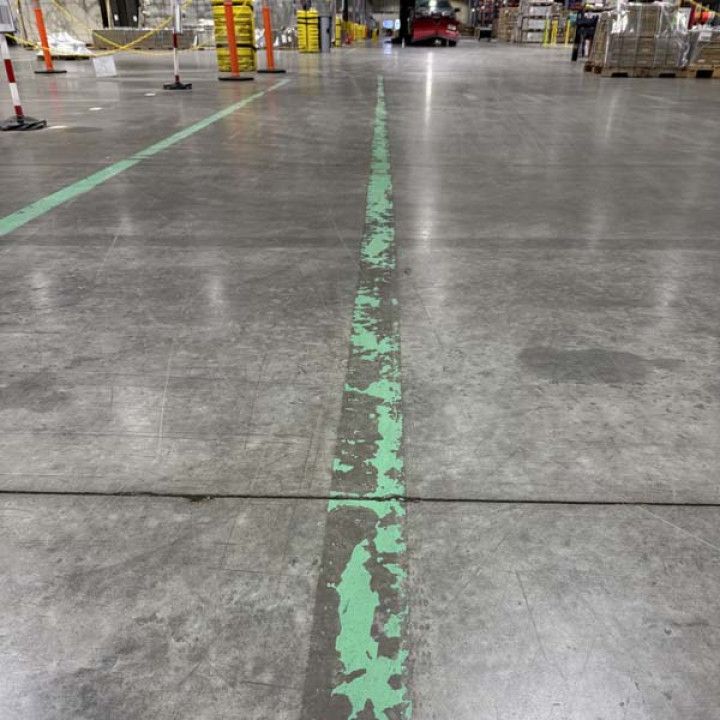 Green painted line on a gray concrete floor in a warehouse setting.
