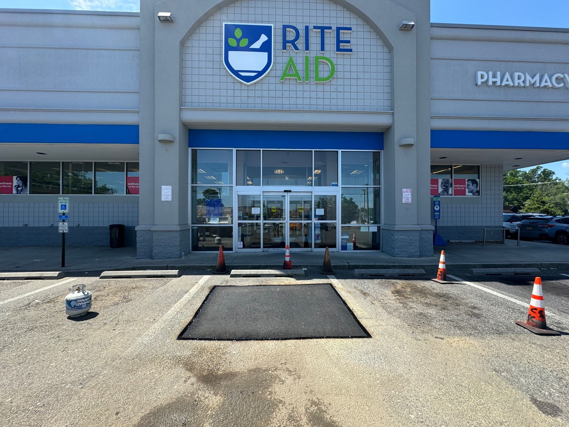 Rite Aid store front with freshly paved asphalt repair. Blue and white facade with automatic doors.