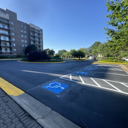 Exterior view of a newly paved parking lot with several blue handicap parking spaces in front of a multi-story building.