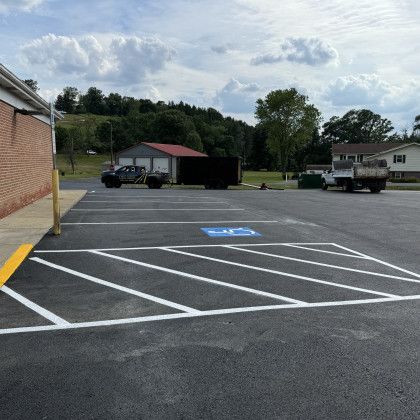 Parking lot with white painted lines and a blue accessible parking symbol. Building and trucks visible.