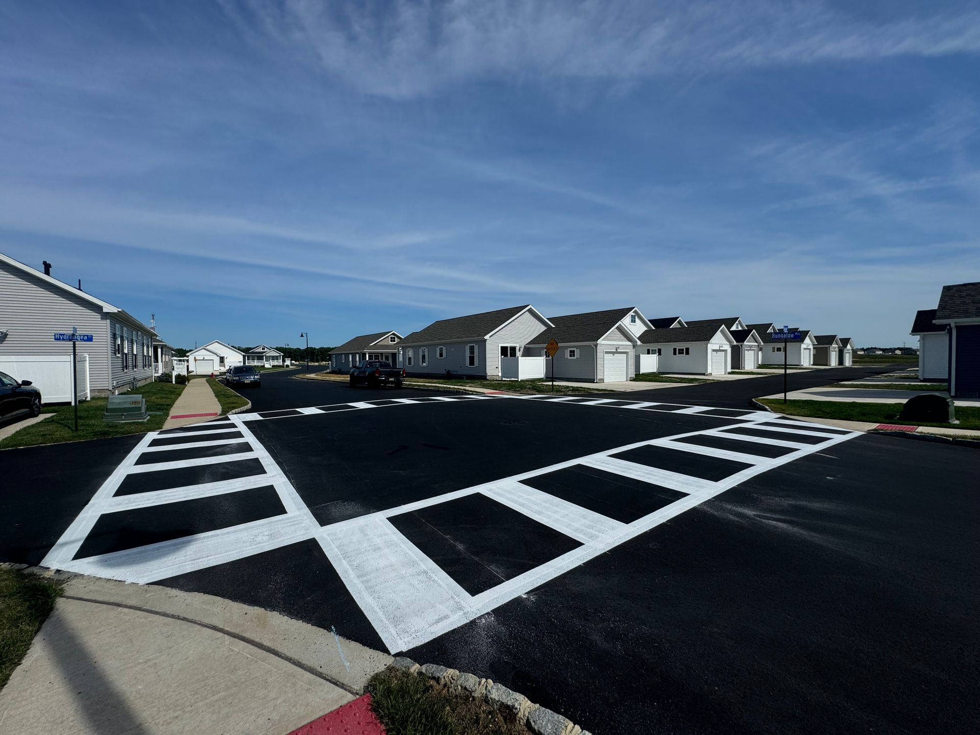 Street with crosswalks leading to houses with white garage doors under a blue sky.