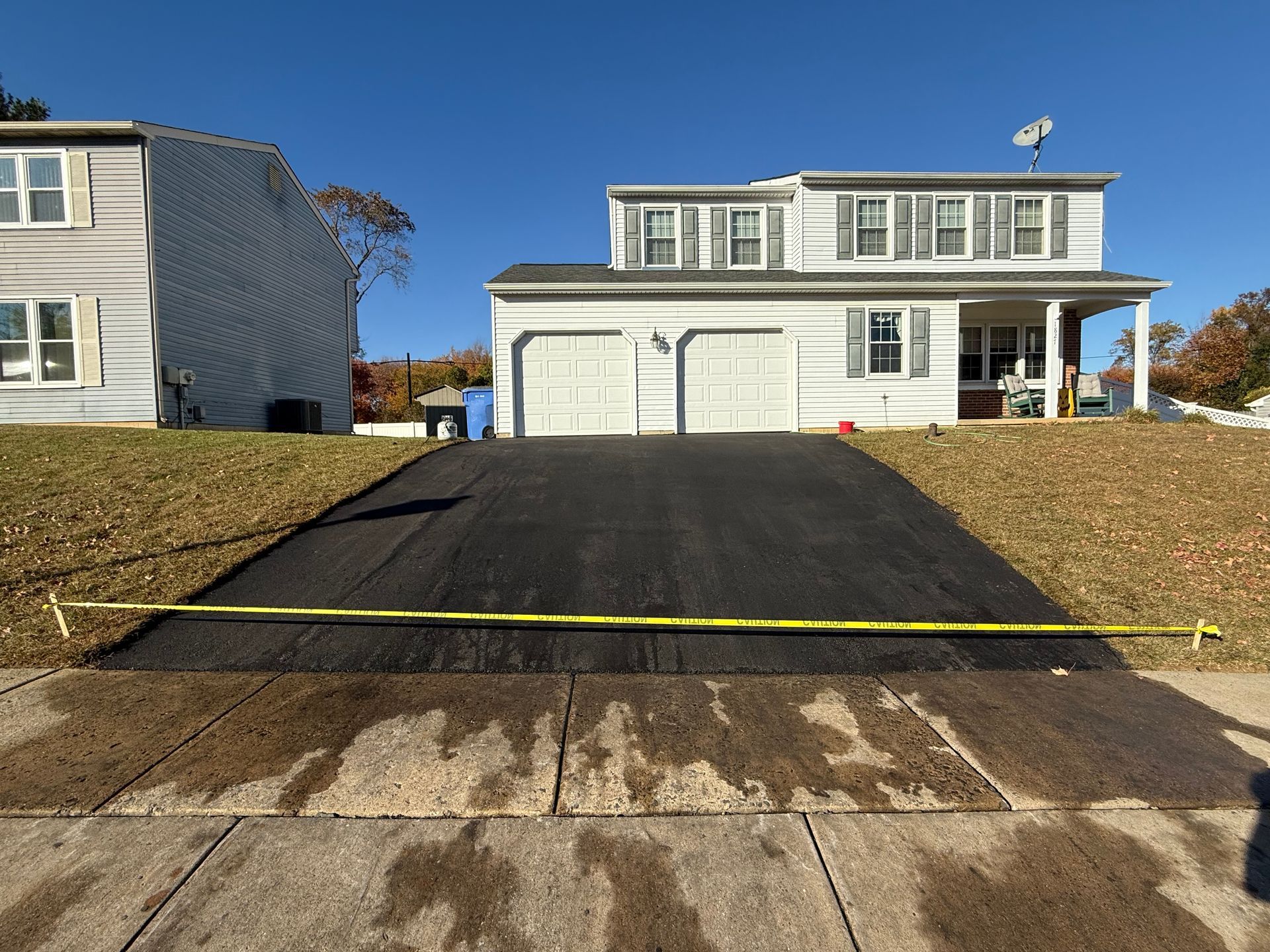 Two-story house with a freshly paved black driveway and yellow caution tape across the front.