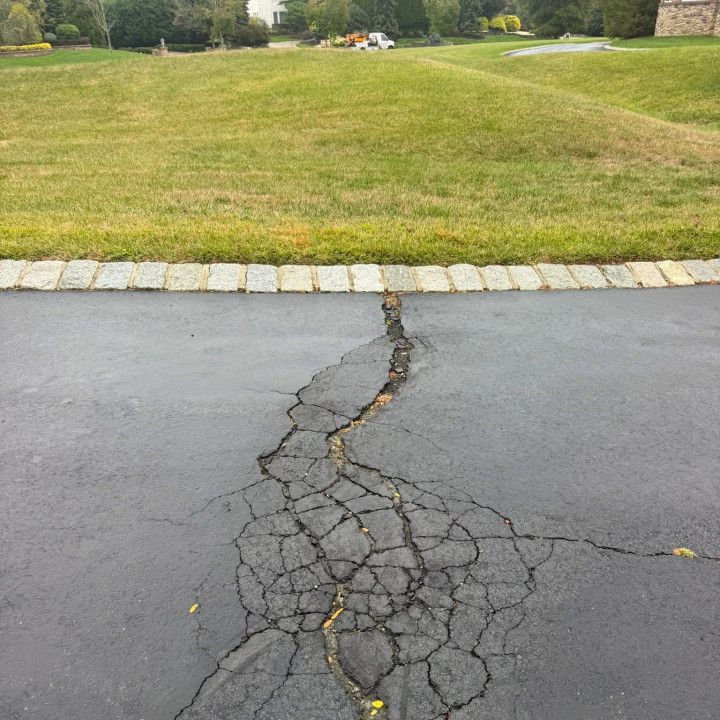 Cracked asphalt driveway with grass lawn in background.