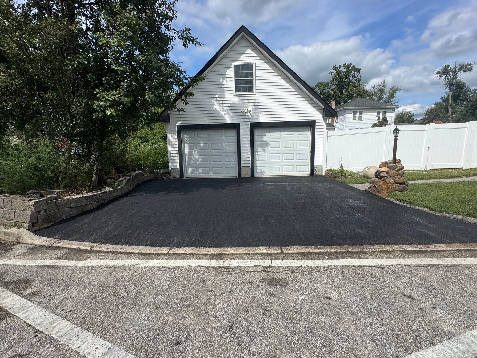 Black asphalt driveway leading to a white two-car garage under a gable roof.