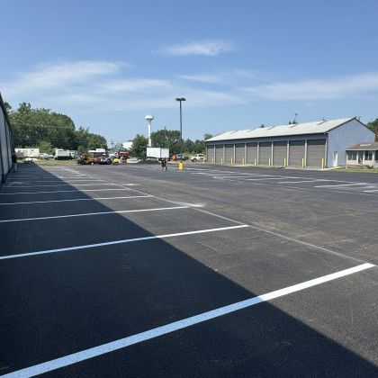 Newly paved parking lot with white painted lines. Buildings and vehicles in the distance.