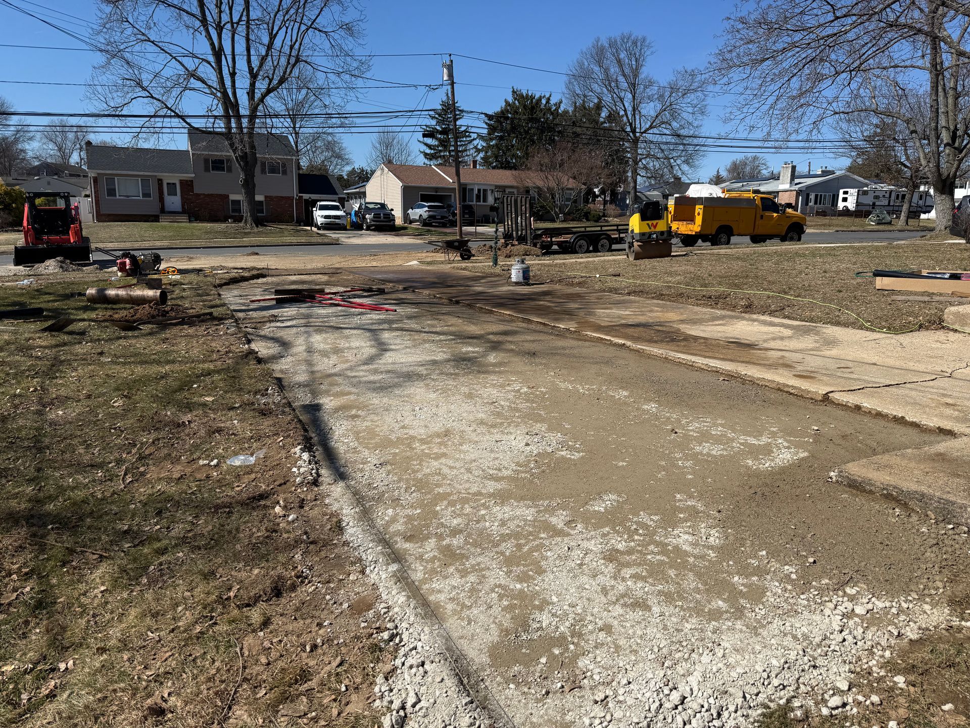 Gravel road under construction in a residential neighborhood, with trucks and equipment under a clear blue sky