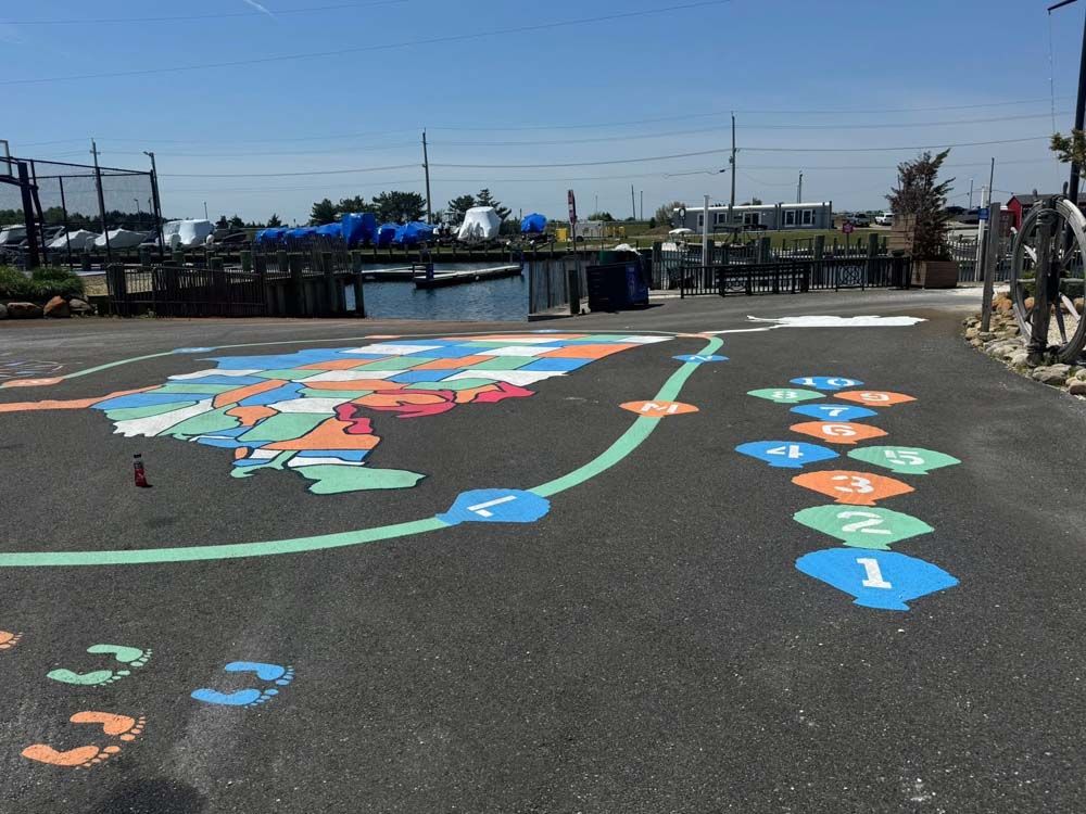 Pavement with painted hopscotch and map of the United States near a waterfront dock, sunny day.