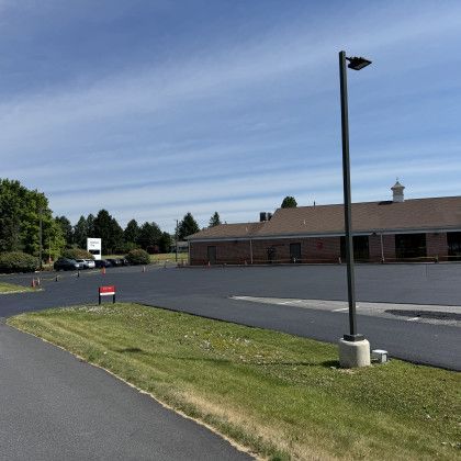 Exterior view of a paved parking lot and a building with a brown roof and a green lawn on a sunny day.