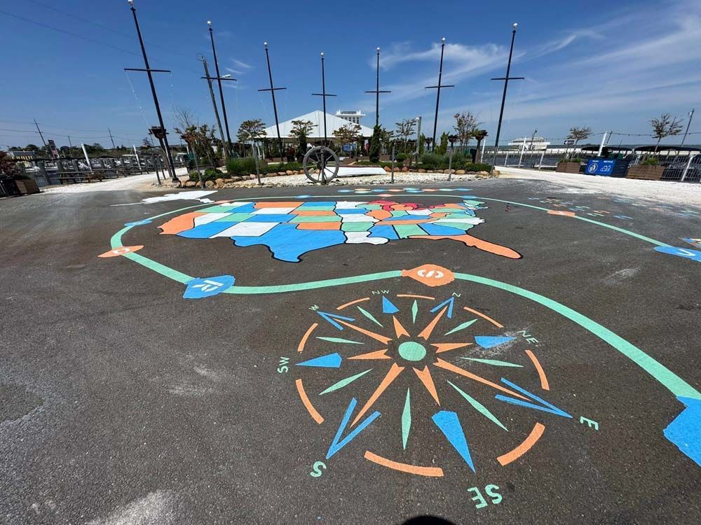 Painted map of the USA with a compass rose on a paved area, under a blue sky, near tall poles.
