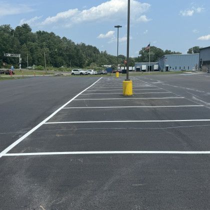 Empty parking lot with freshly painted white lines. A few cars and buildings are in the background. Blue sky.