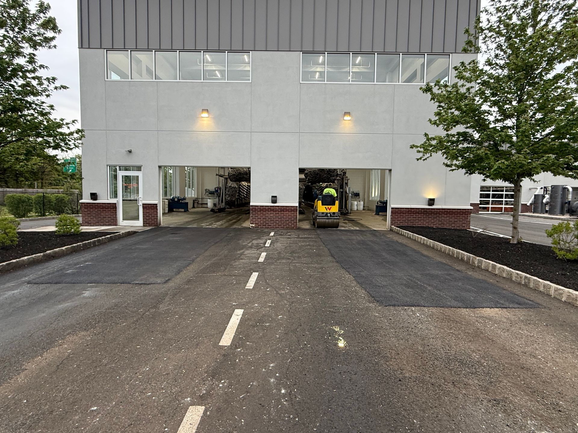 Industrial building entrance with open bays, a parked forklift, and a paved driveway under overcast skies