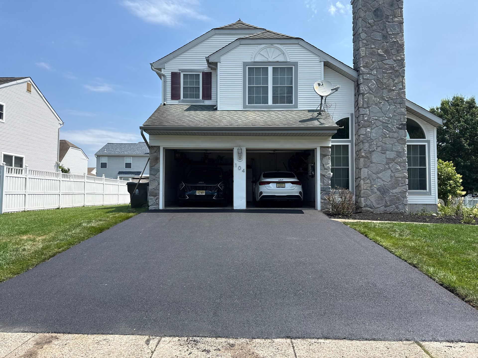 White detached garage with two doors, black driveway, and a small front lawn under a cloudy sky.