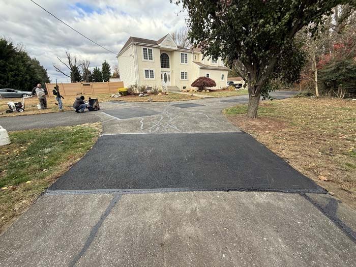 Driveway leading to a beige house with workers and paving equipment in a suburban yard