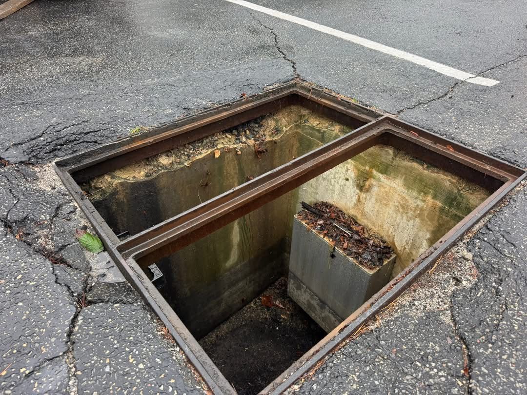 Open storm drain in cracked asphalt road with metal grating across the opening