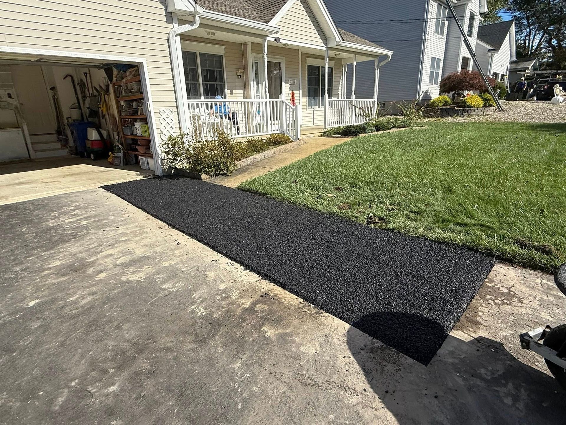 Black asphalt patch on a driveway beside a green lawn and a house porch.
