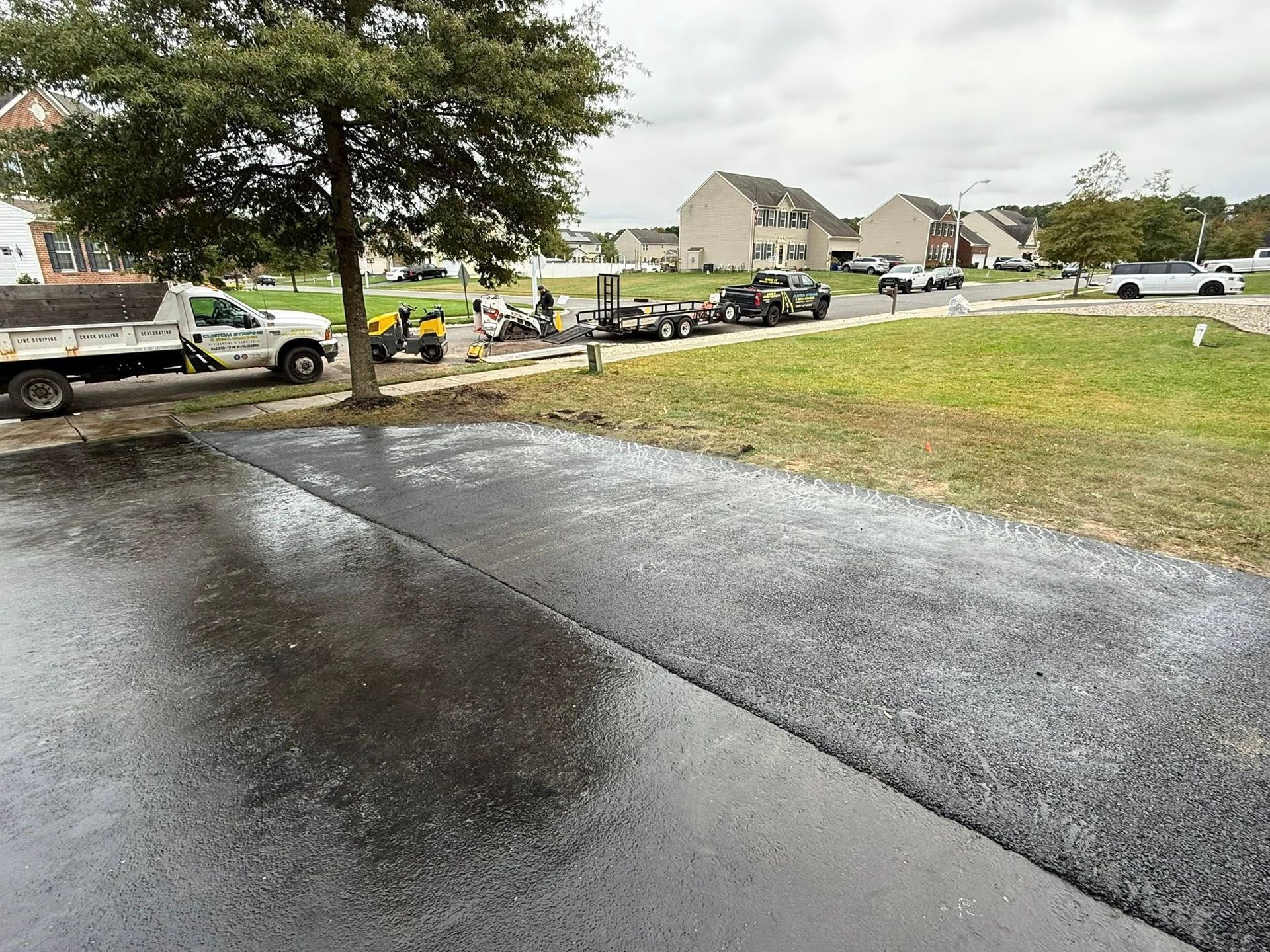 Rainy suburban driveway with parked vehicles, grassy yard, and houses in the background.
