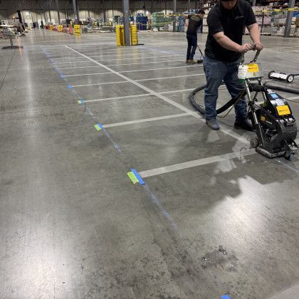 Person using a concrete grinder in a warehouse, grinding floor lines.