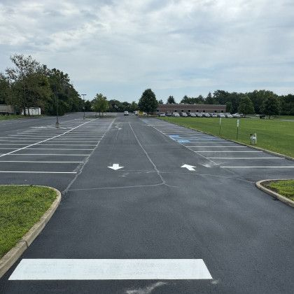 Empty parking lot with directional arrows and accessible parking spaces, next to a grassy area and building.