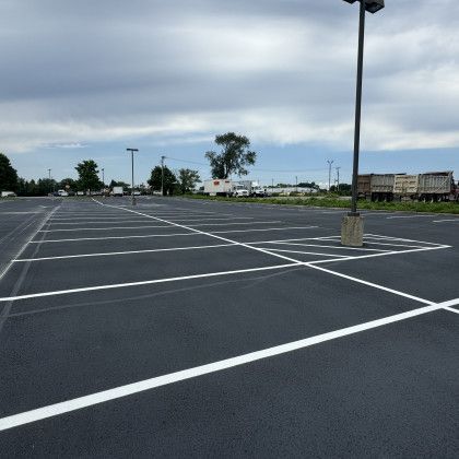 Empty parking lot with white painted parking space lines on dark asphalt under a cloudy sky.